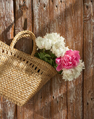 Fototapeta na wymiar Flowers of pink red and white peonies in wicker basket on wooden table against wooden background