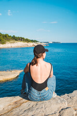 young pretty woman sitting on the cliff looking at sea