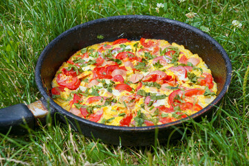 scrambled eggs omelet with sausages and tomatoes, cooked on fire, in nature