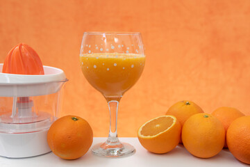 Vaso de jugo de naranja natural y exprimidor sobre fondo naranja