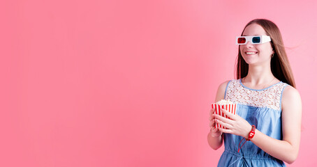 Smiling teenager girl wearing 3D glasses eating popcorn isolated on pink background