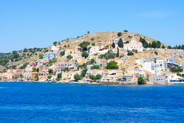 A lot of tiny colorful houses on the rocky shore of Mediterrenean sea on Simy greek island in sunny summer day, tourism on exotic islands