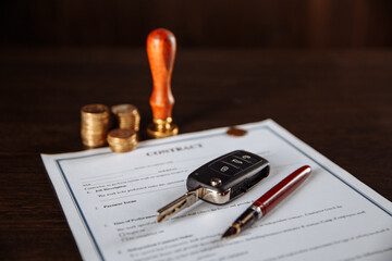 Contract for car purchase, stamp, pen and car key on wooden table.