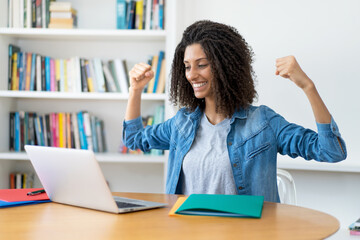 Cheering latin female student with curly hair at computer