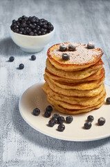 Homemade pancakes with blueberries in a plate on a light wooden table.