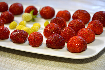 Strawberry berries are on a plate. Red and yellow berries close-up.