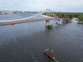 Aerial drone view. A pirate motor boat sails under bridge along the Dnieper River in Kiev.