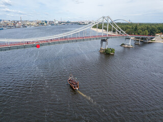 Aerial drone view. A pirate motor boat sails under bridge along the Dnieper River in Kiev.