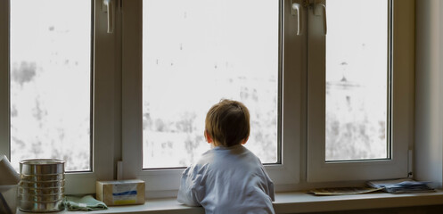 A little boy looks out the window. The street is bright and sunny. Cold weather