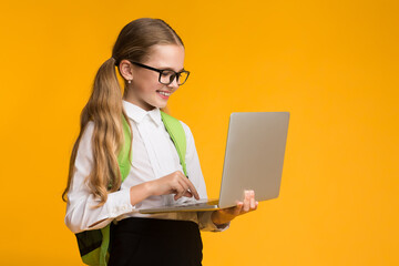 Smiling Schoolgirl Using Laptop Studying Standing On Yellow Studio Background