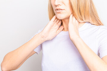 Female checking thyroid gland by herself. Close up of woman in white t- shirt touching neck with...