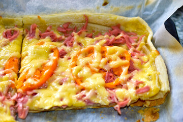 Homemade pizza with meat and yellow tomatoes on a baking sheet