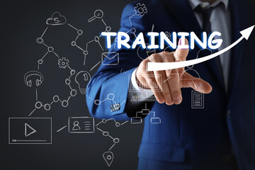 Businessman pointing at virtual screen with inscription TRAINING on dark background, closeup