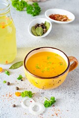 Homemade chicken (bone) broth/bouillon with vegetables, spices and herbs in a bowl (cup) on a light background. Natural collagen of animal origin. Liquid broth from meat, fish, vegetables.