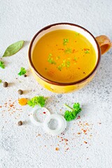 Homemade chicken (bone) broth/bouillon with vegetables, spices and herbs in a bowl (cup) on a light background. Natural collagen of animal origin. Liquid broth from meat, fish, vegetables.