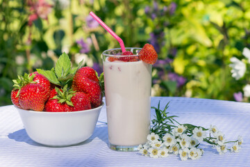 Delicious and nutritious milkshake with strawberries in a glass glass on the table.