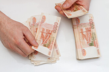 A man's hand counts and shifts a large number of five thousand rubles bills into a stack