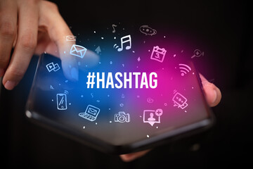 Businessman holding a foldable smartphone with #HASHTAG inscription, social media concept