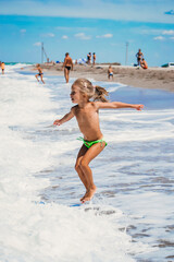 Small girl jump above the waves, happiness of summertime and holiday in summer period. Sand coastline and white waves on the beach. Enjoy of summer days with girl.