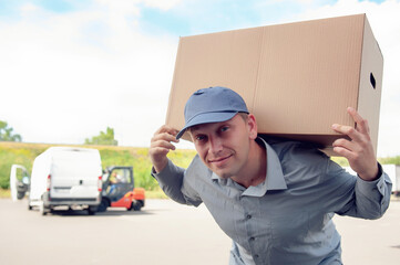 A man in a gray suit in his hands with a cardboard box against the background of the van. Concept on the topic of postal delivery.