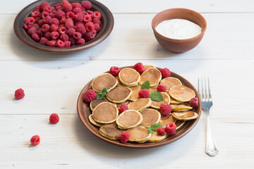 Pancake cereals with yogurt and ripe fresh raspberries in a brown plate on a white wooden table. Delicious Breakfast