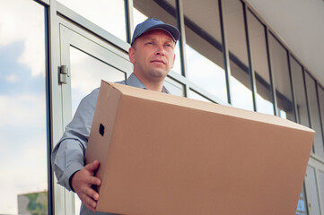 A man in a gray suit in his hands with a cardboard box against the background of the supermarket. Concept on the topic of postal delivery.