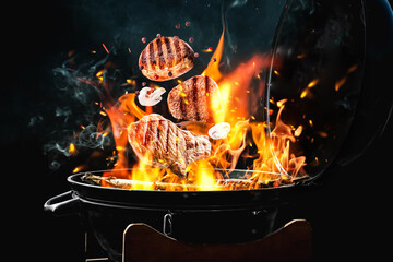 Meat and mushrooms falling onto barbecue grill with flame against black background, closeup - obrazy, fototapety, plakaty