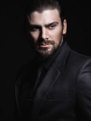 Young white Caucasian man on a black background in a black jacket, shirt and black tie looks out...