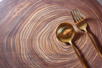 The golden fork and spoon lies on a slice of a tree. wooden table. With copy space.