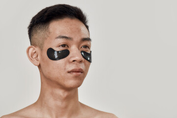 No dark circles. Portrait of shirtless young asian man with black patches under the eyes looking away isolated over white background. Beauty, skincare routine, cosmetology for men