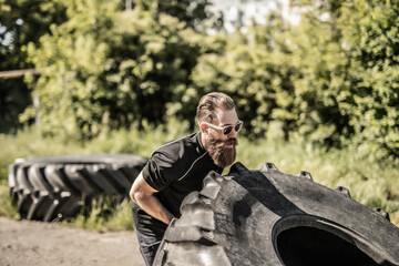 Full length side view of young man athlete flipping large tire outside gym - Powered by Adobe