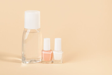 Bottle with nail varnish remover, white and pale pink nail polish on a powdery color background. Manicure, pedicure, nail care products. Copy space.