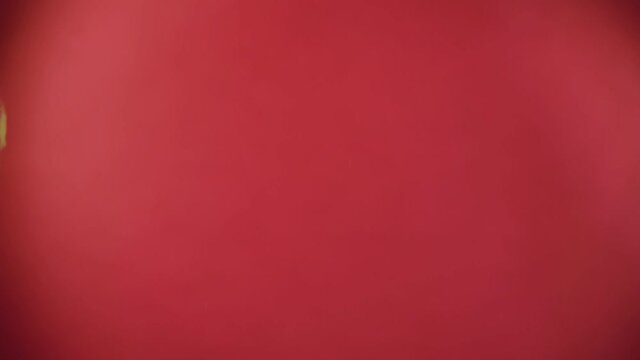 Two large ripe red apples are flying towards each other, colliding on the red background and raising splashes of water in slow motion