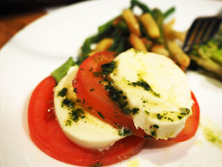 sliced ​​tomato with white soft cheese and garlic dressing on a white round plate with other dishes side view