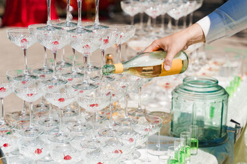 The waiter pours champagne into crystal glasses close up. Sparkling wine pouring in wine glass at summer day. Catering for business people