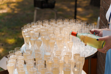Waiter pours champagne in disposable plastic wine cup. Pouring sparkling wine into wine glass on...