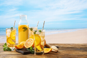Tasty refreshing drink on wooden table against sandy beach