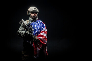American soldier in military uniform with a gun holds the USA flag against a dark background, the...