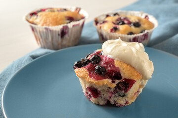 Sweet muffin with black currants and whipped cream on a blue plate, homemade fruity dessert, copy space