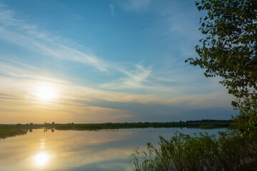 Sunset over the river in summer. The sun goes down the horizon. River landscape in summer, fog view