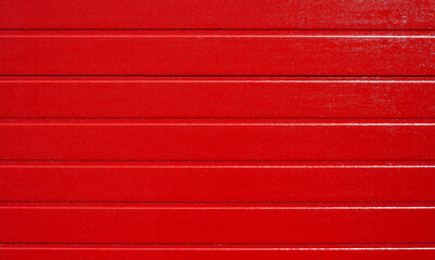 Red wooden background, horizontal striped texture. Folding garage door made of metal profile, red carbon. Red corrugated wall