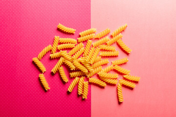 Spiral pasta scattered on a dark pink and light pink background  