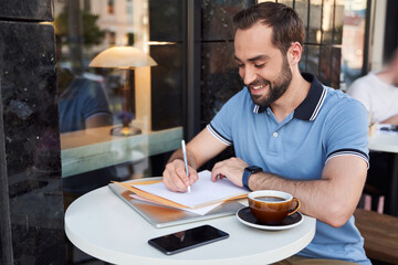 Happy young man with gadgets drinking coffee in cafe