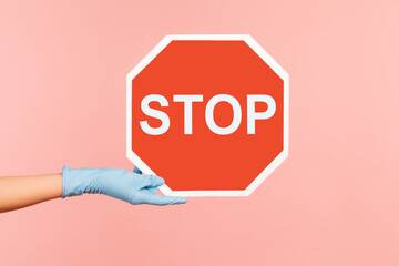 Profile side view closeup of human hand in blue surgical gloves holding and showing Stop sign....