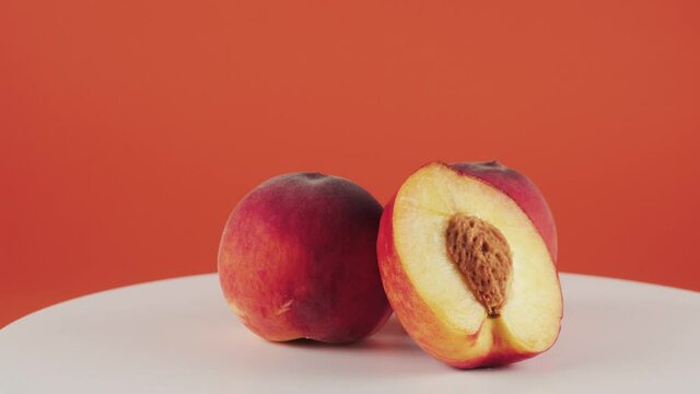 Close up, half of nectarine and two peaches on rotating table isolated on orange background. Concept of fruits, healthy food.