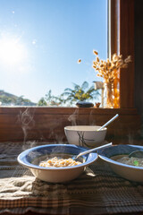 Bowls of steaming hot porridge sitting on the kitchen bench of a sunny country kitchen on a winter morning with ferns seen through the window outside 