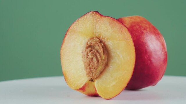 Close up, two half of juicy nectarine on rotating table isolated on green background. Concept of fruits, healthy food, organic product