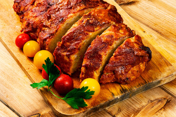 Classic meatloaf on a cutting board on a wooden background. In the background are red and yellow cherry tomatoes, parsley, ears of wheat