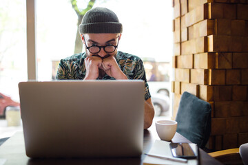 Male hipster playing in online casino on laptop and hoping his bet will win