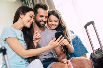 Beautiful happy excited family with a backpack and suitcases in modern hotel watching on smart...